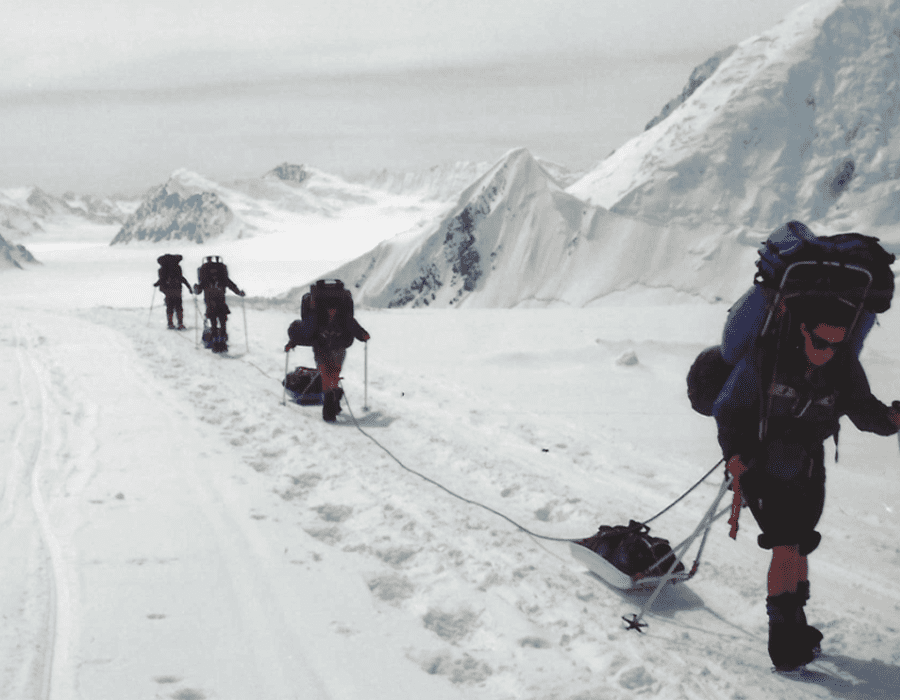 Explorers trekking through snowy mountainous terrain with sleds.