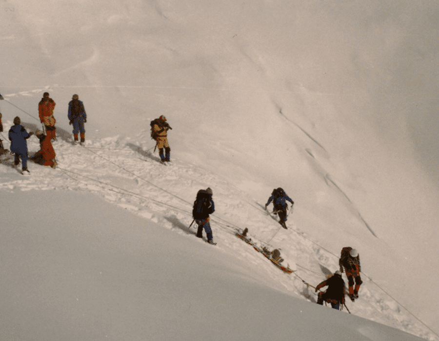 Group of climbers ascending a snowy mountain slope in harsh conditions.