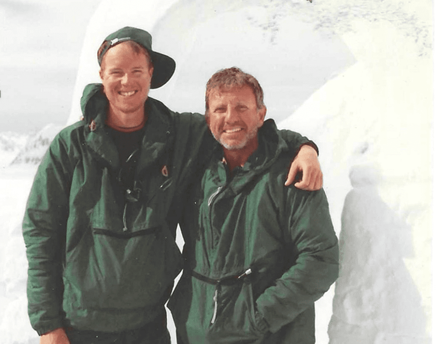 Two men in green jackets smiling with a snowy background.