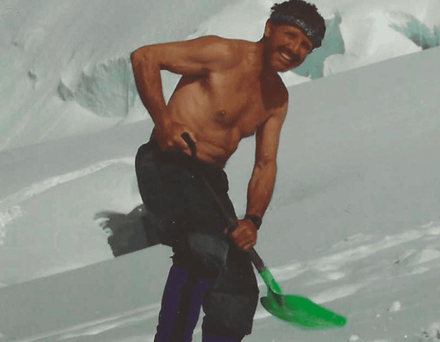 Man smiling while playing beach cricket with a green bat.