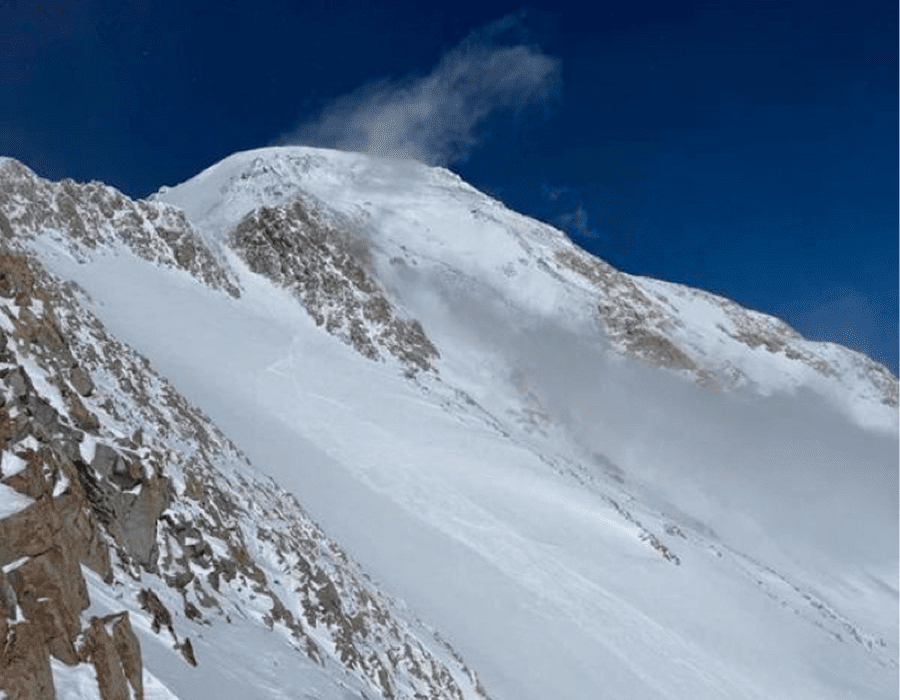 Snow-covered mountain peak with strong winds blowing snow off the summit.