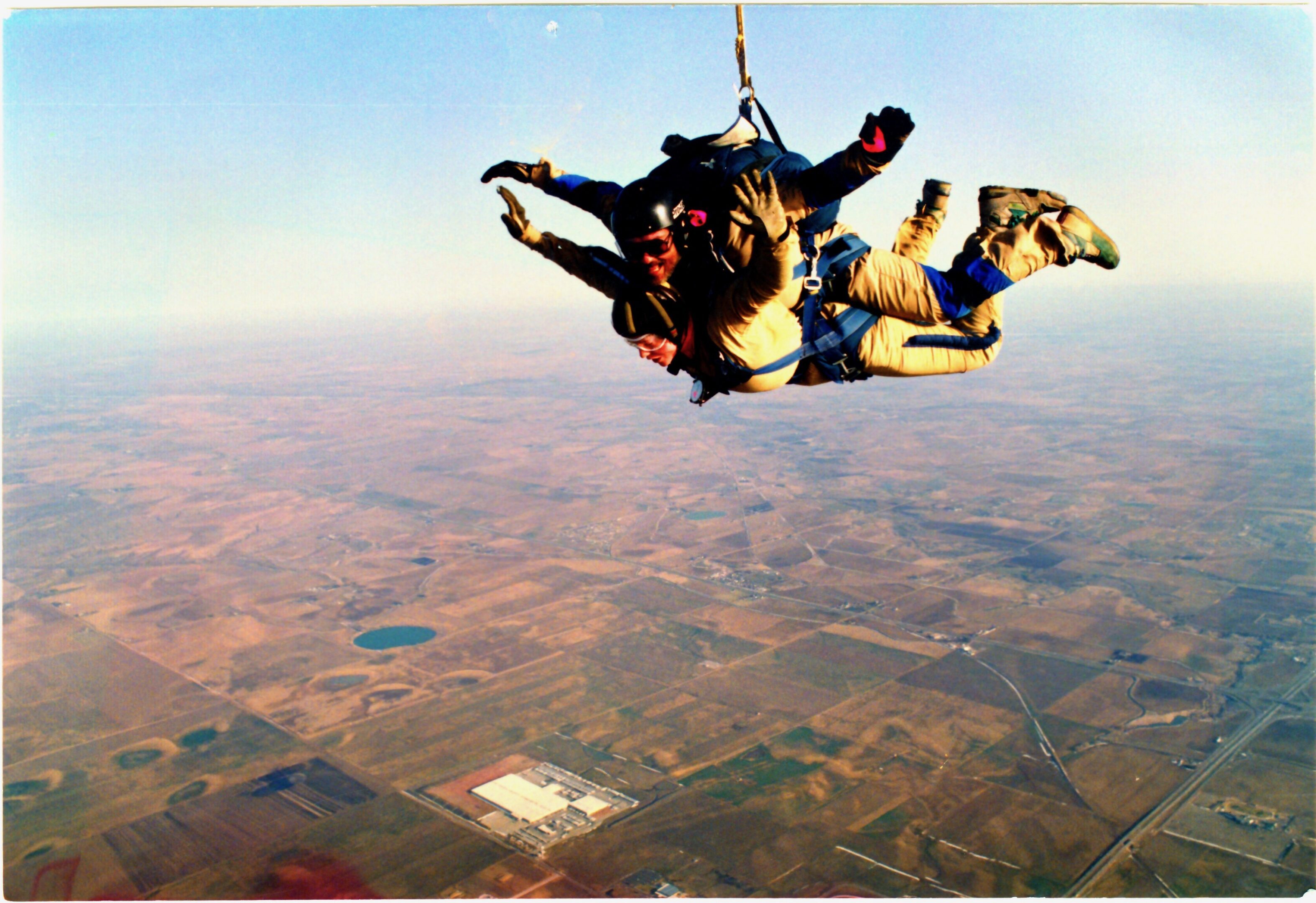 Two people tandem skydiving over a rural landscape.