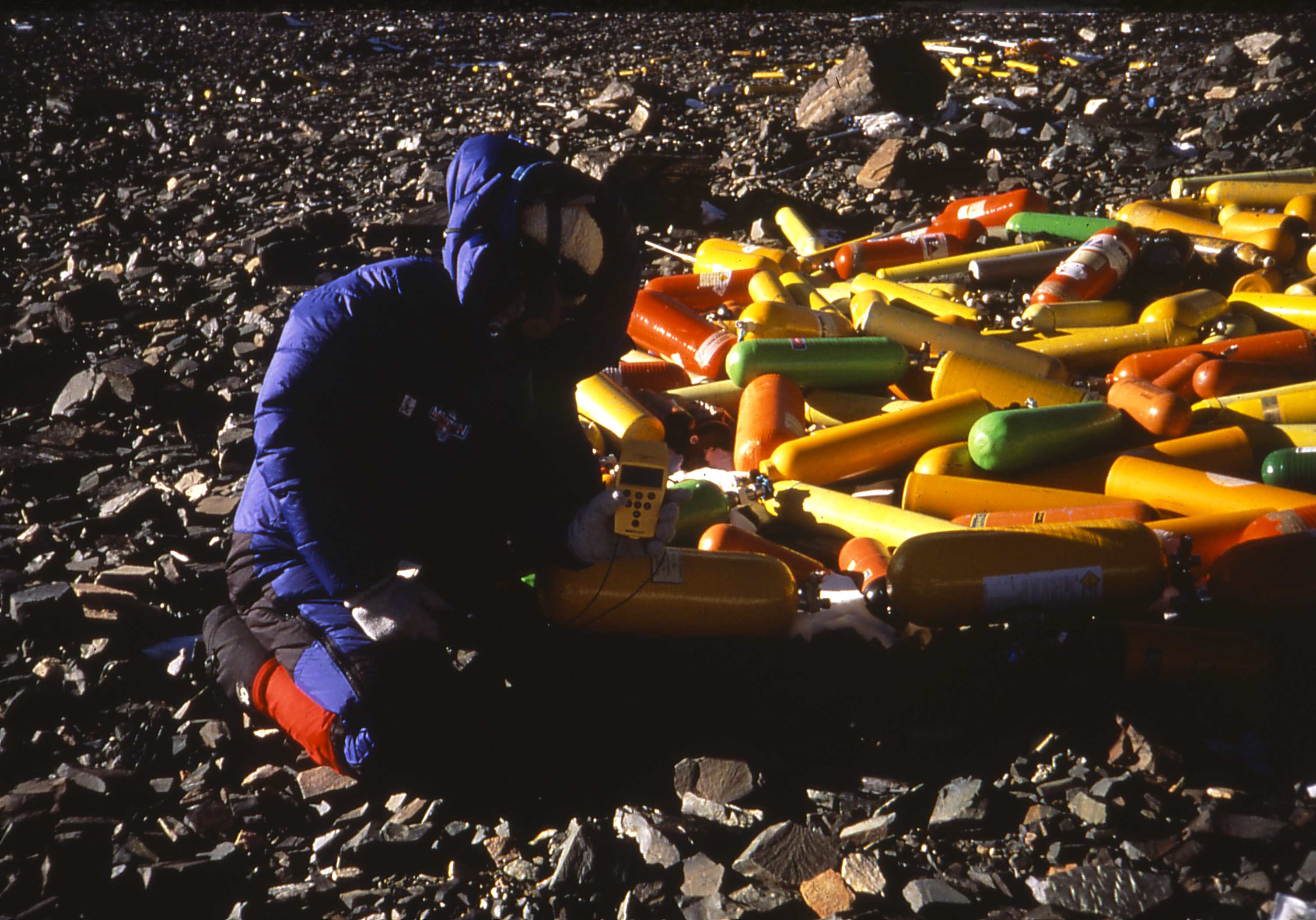 Researcher with vibrant equipment on stony terrain.