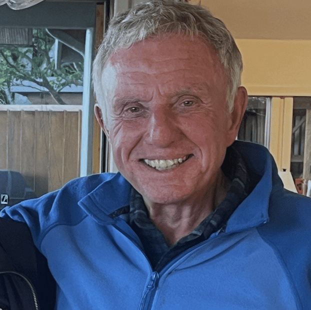 Smiling elderly man wearing a blue jacket indoors.