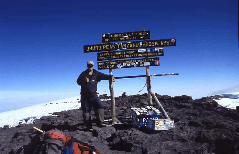 Person posing by the summit sign at Mount Kilimanjaro's Uhuru Peak.