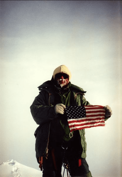 Person in heavy winter gear holding a tattered American flag.