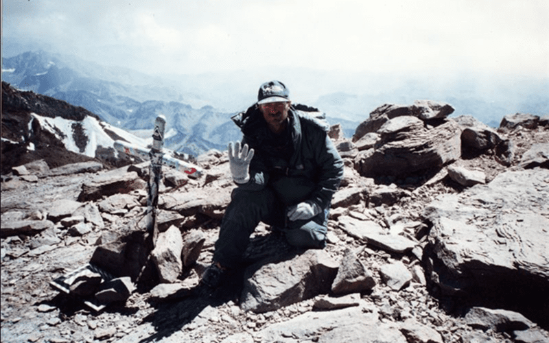 Man sitting on rocky terrain with mountains in the background.