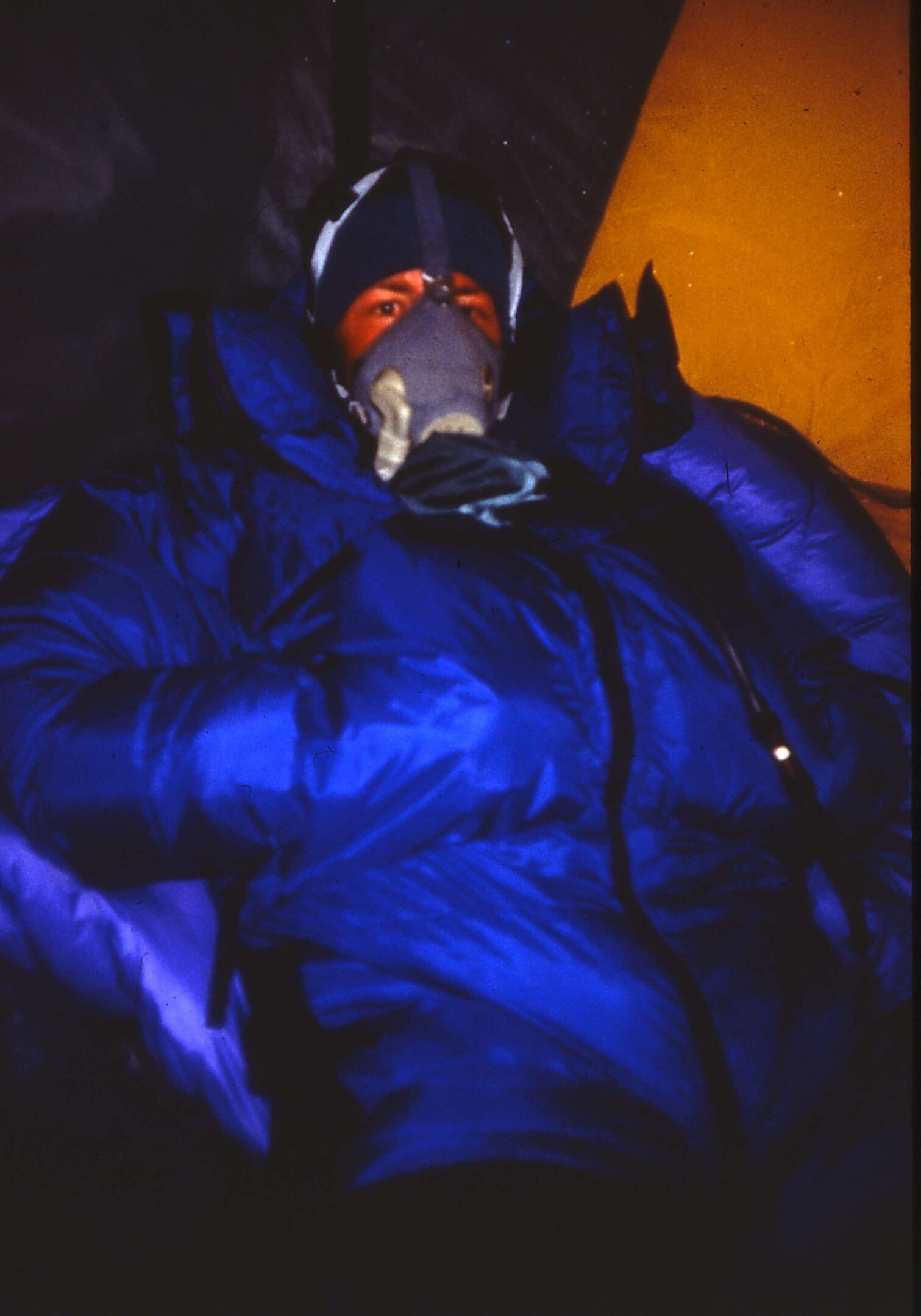 Person wearing a dark blue puffer jacket with a gas mask in low light.