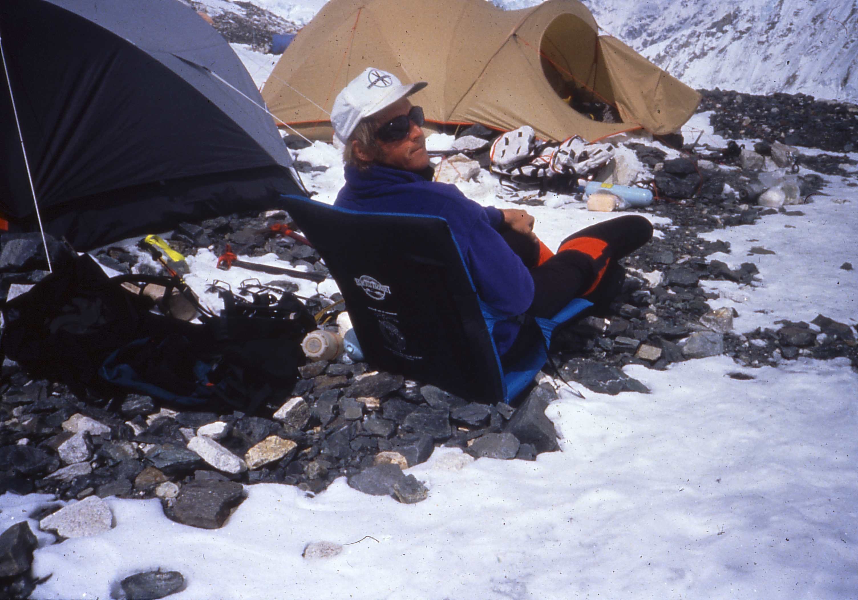A person sitting on a chair in snowy mountainous terrain near tents.