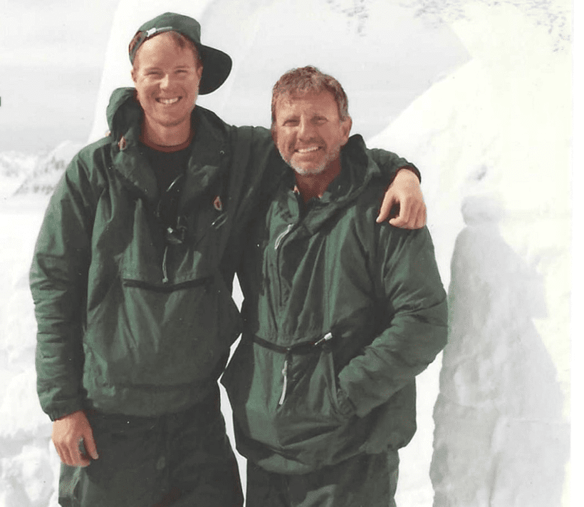 Two men in green jackets smiling and posing together outdoors.