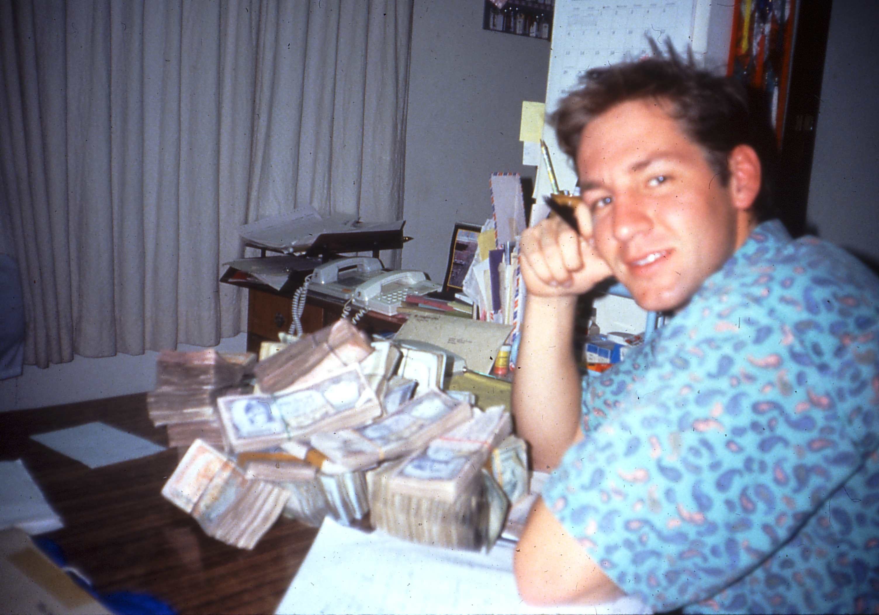 Man posing with large stacks of money on a table.