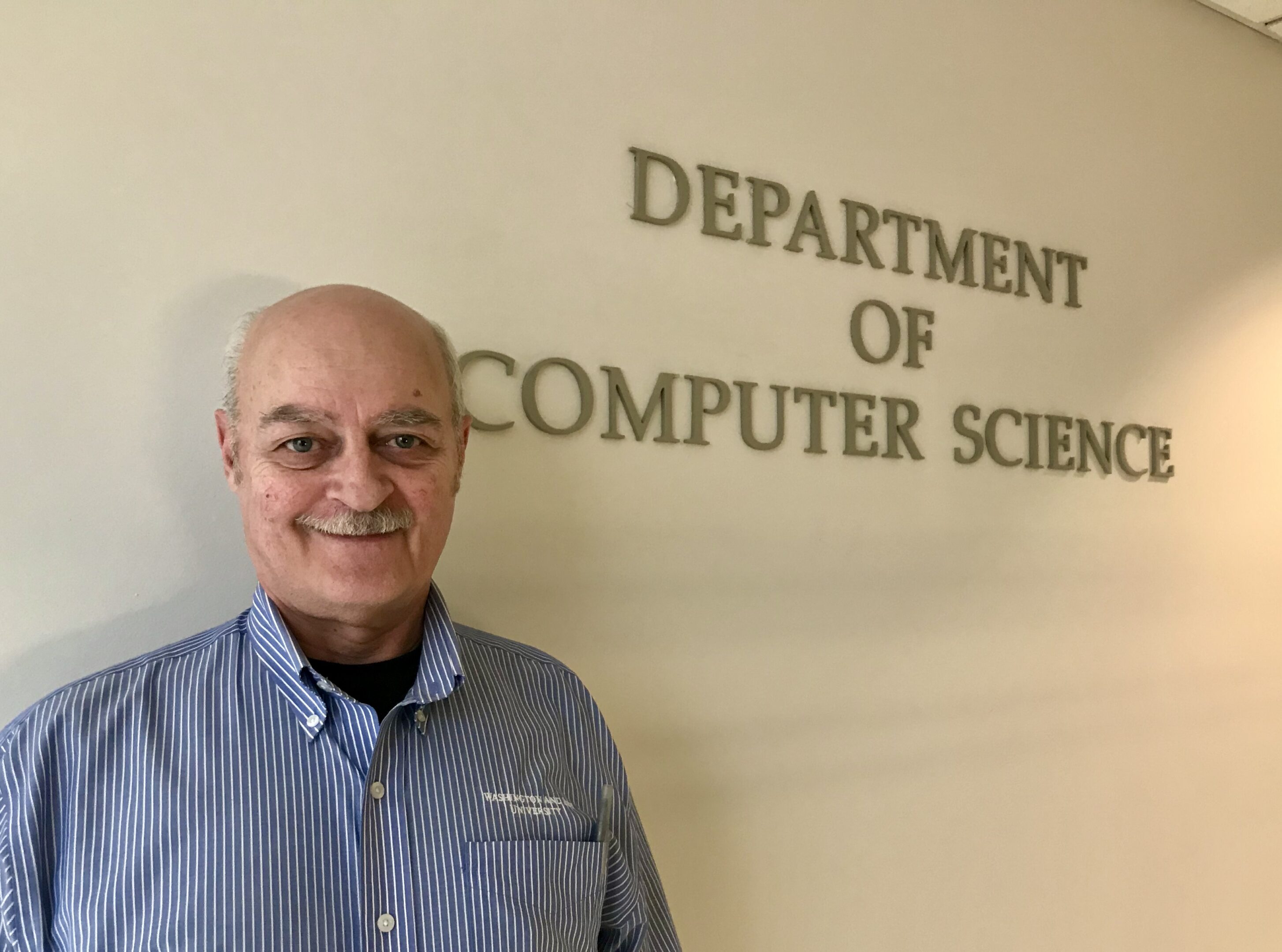 Smiling man standing in front of a Department of Computer Science sign.
