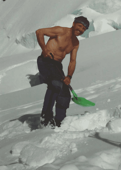 A shirtless man shoveling snow outdoors on a sunny day.