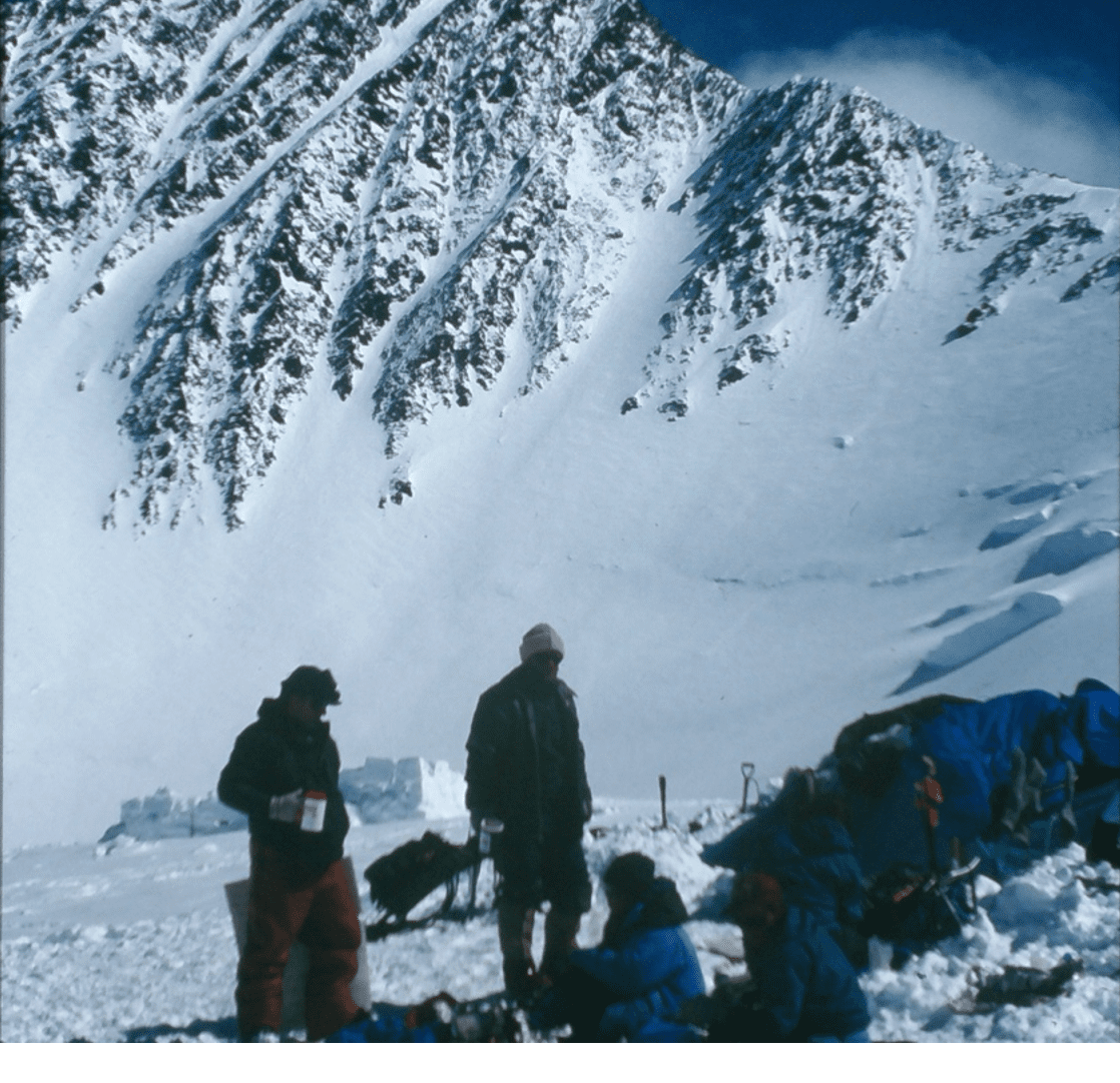 Two people in snowy mountain terrain with camping gear.