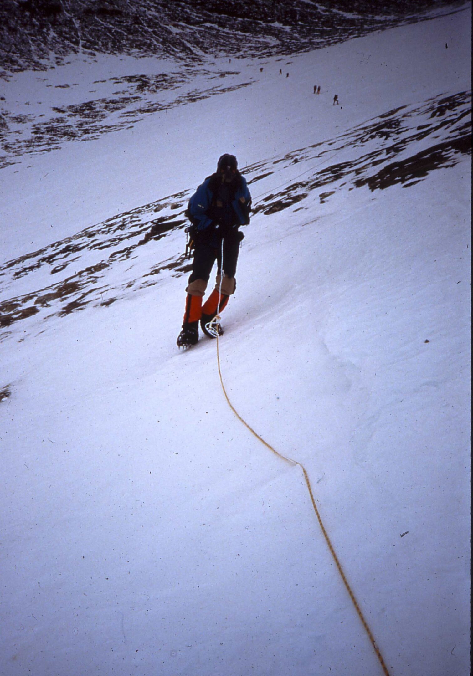 A climber ascending a snowy mountain slope with a rope.
