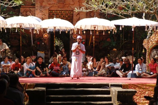 A musician performs on stage under white umbrellas with an audience watching.