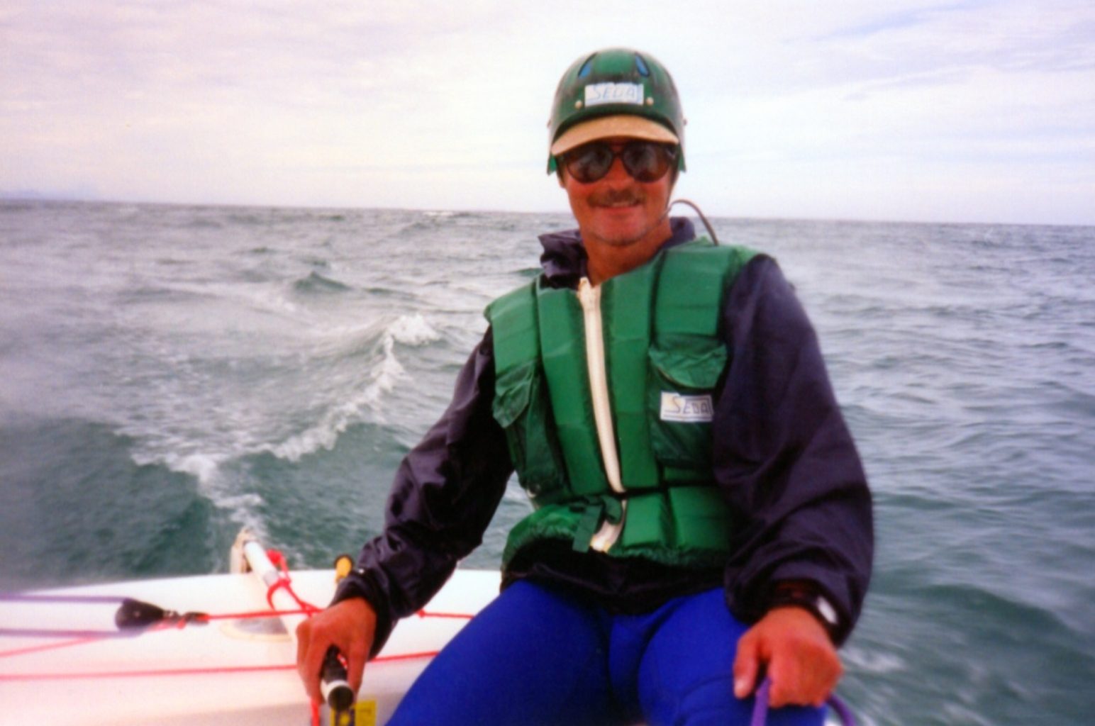 Person wearing a life jacket and cap on a boat in rough waters.