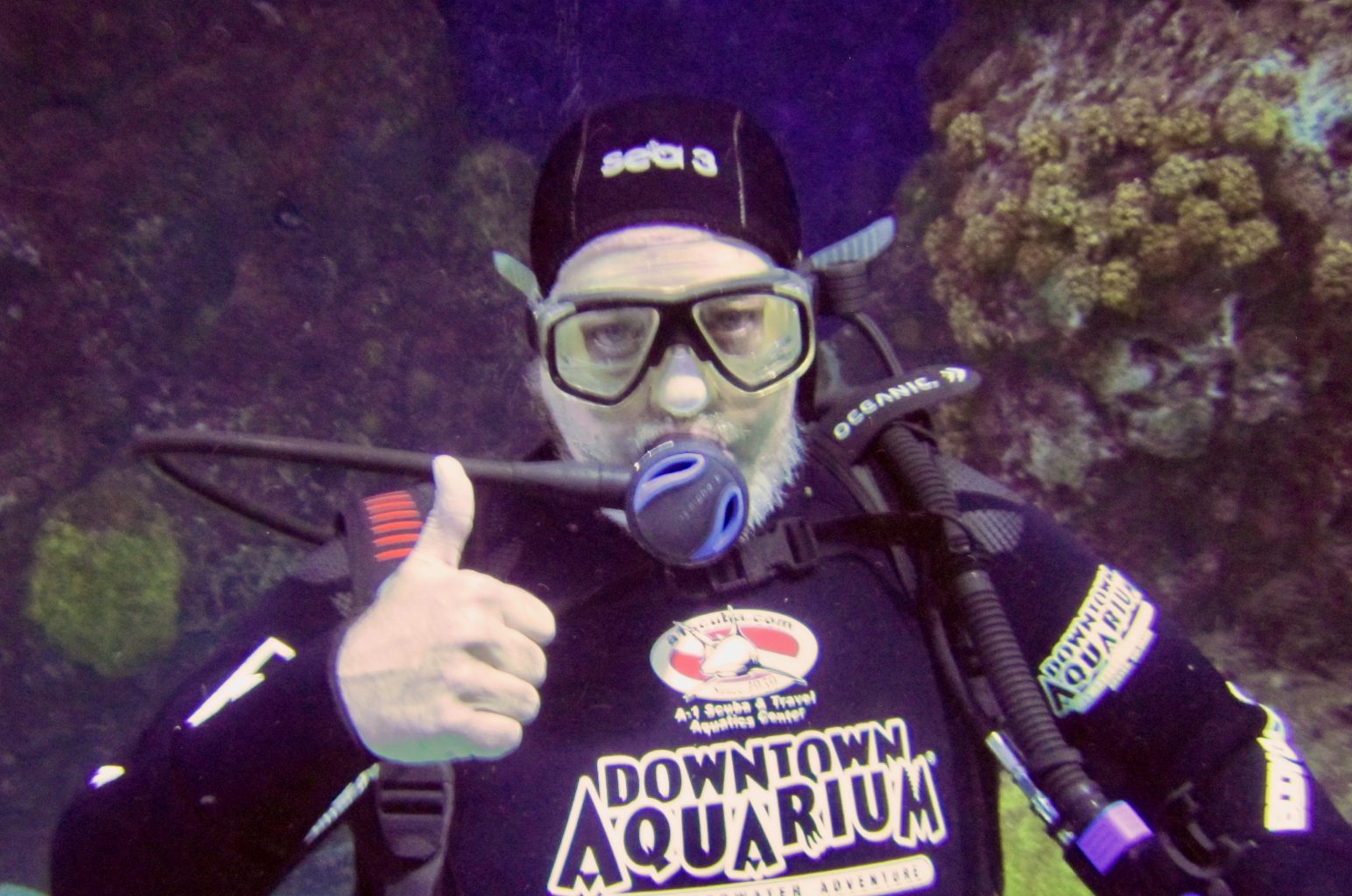 A scuba diver gives a thumbs up underwater near coral.