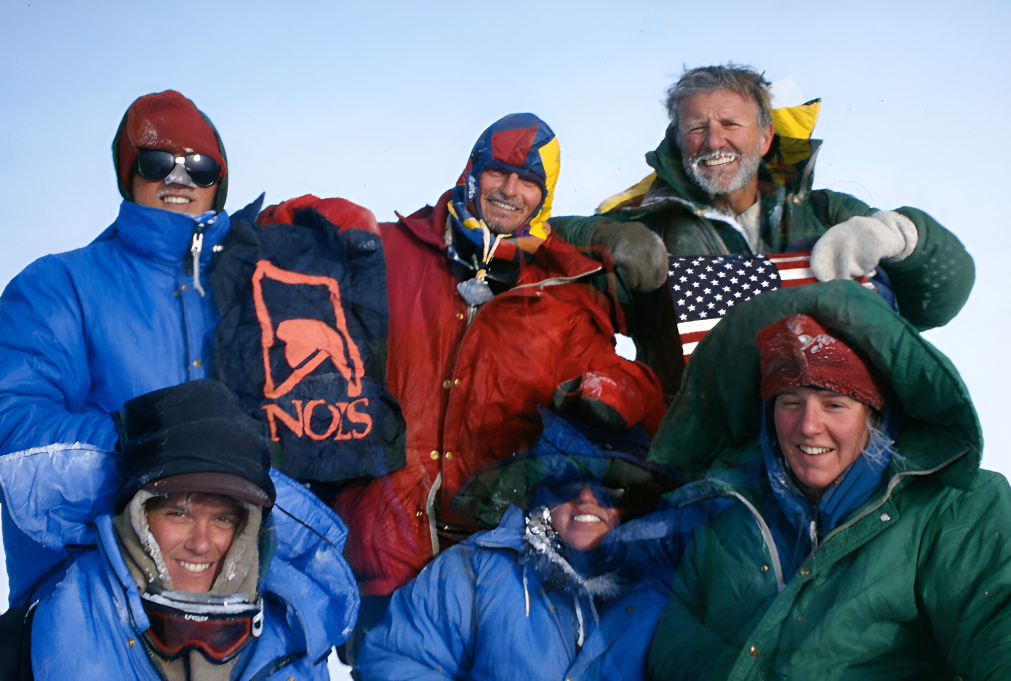 Group of happy climbers in colorful winter gear posing on snowy mountain.
